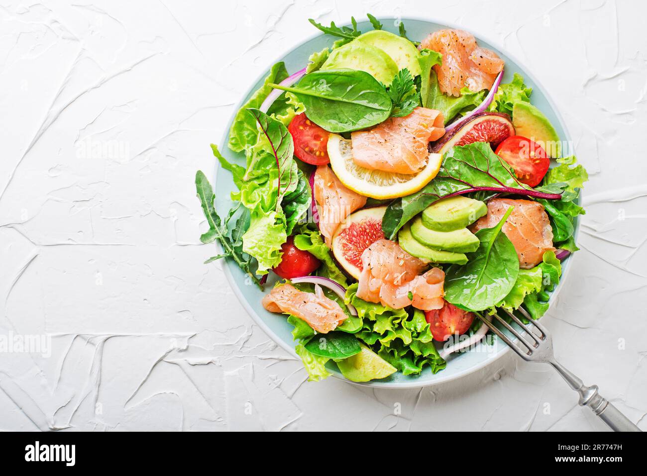 Insalata verde fresca con salmone affumicato, pomodori ciliegini, fichi e avocado su sfondo bianco Foto Stock