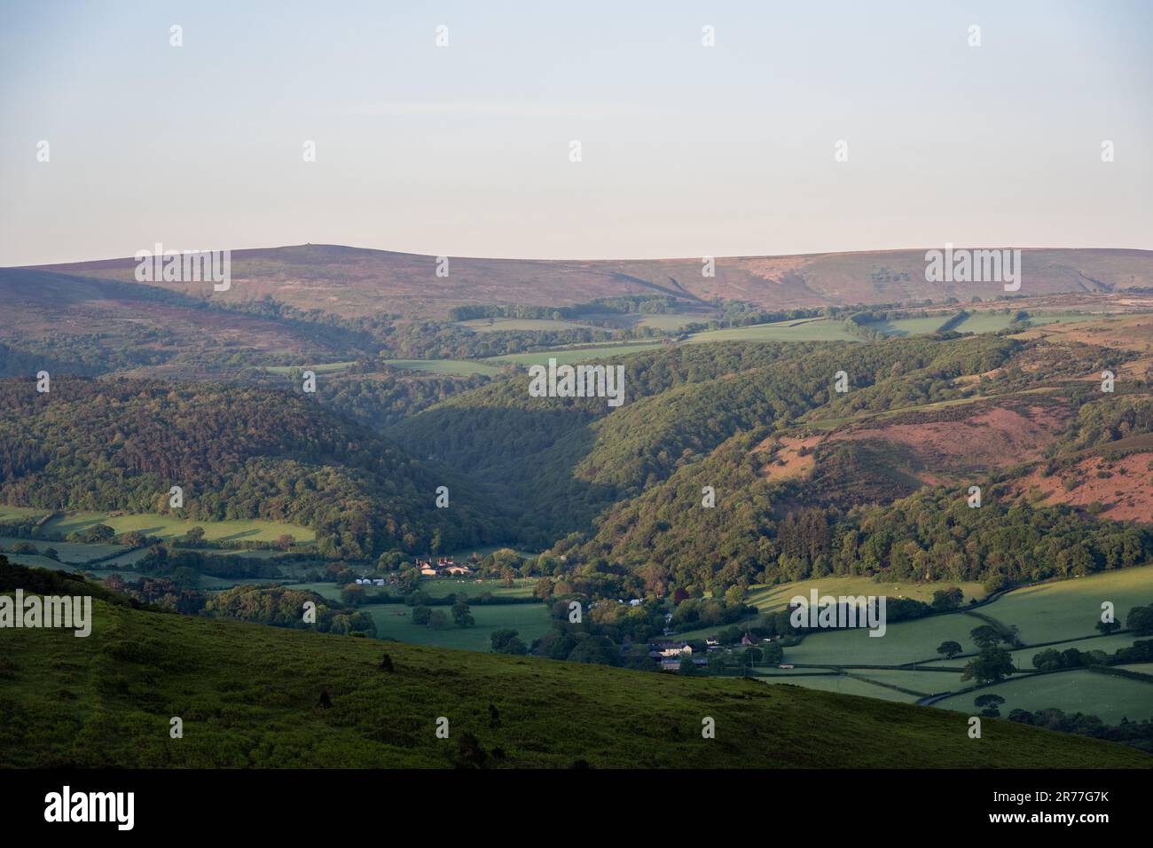 Il sole mattutino splende su Dunkery Beacon e su altre colline di Exmoor sopra il villaggio di Horner nel Somerset occidentale. Foto Stock