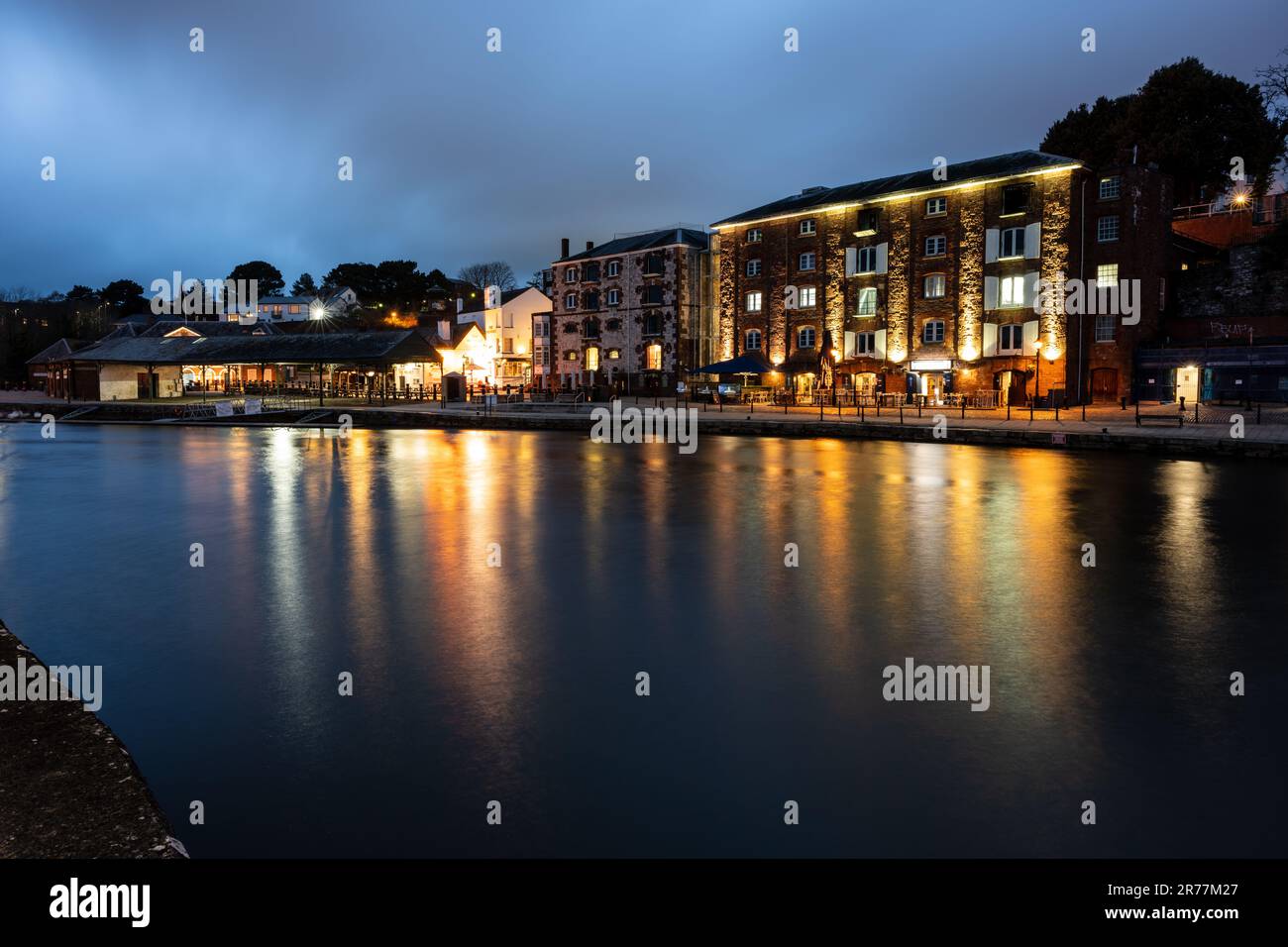 I magazzini convertiti sono illuminati di notte al molo rigenerato di Exeter sulle rive del fiume exe. Foto Stock