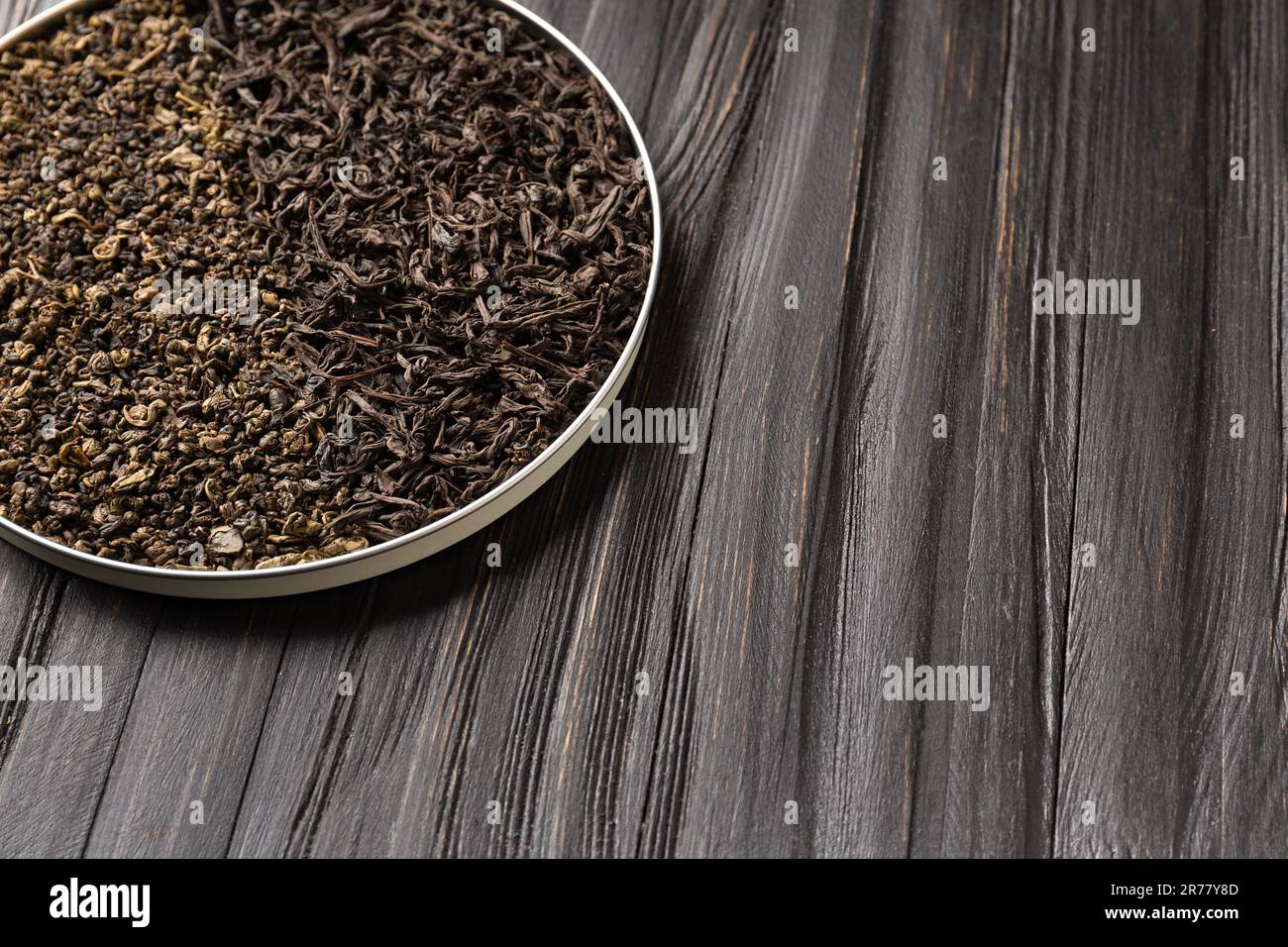 Composizione concettuale di foglie secche di tè nero e verde in una ciotola rotonda su uno sfondo di legno con spazio per il testo. Tè verde e nero al buio Foto Stock