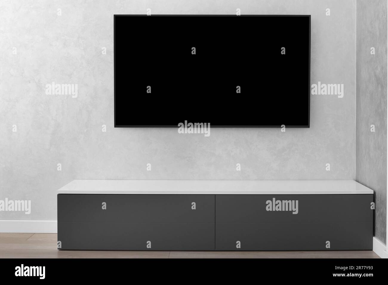 Parte dell'interno di un moderno soggiorno, una Smart TV LED su una parete grigia, un armadietto grigio, un tappeto. Minimalismo negli interni. Foto Stock