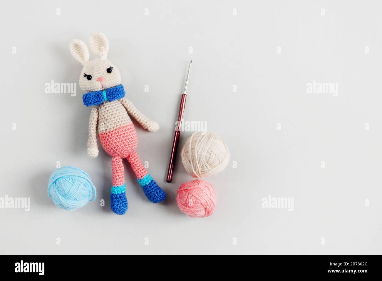 Coniglietto giocattolo lavorato a maglia con palla di fili e gancio a maglia su sfondo grigio. Articoli e accessori per bambini. Vista dall'alto, disposizione piatta. Foto Stock