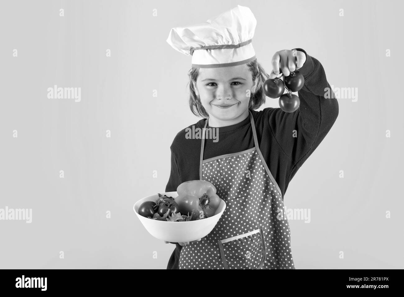 Il cuoco del capretto tiene il pomodoro. Ritratto di bambino piccolo in uniforme di cuoco. Chef ragazzo isolato su sfondo studio. Bambino carino per essere uno chef. Bambino vestito come un Foto Stock