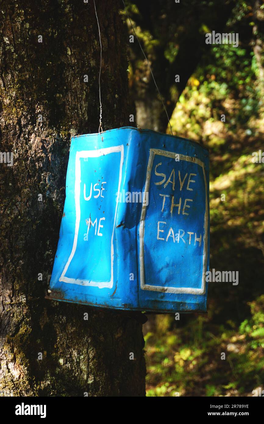 La lattina riciclata pastigliata contenitore di lettiera pende da un albero lungo un sentiero escursionistico in Bhutan. "Salva la Terra" è dipinto sul lato della lattina blu. Foto Stock