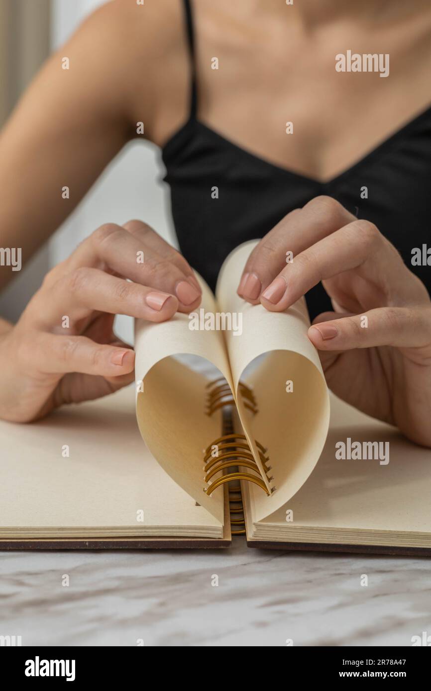 piegare il foglio di carta da un taccuino formando un cuore, eseguendo origami, attività creativa e artistica, dettagli di oggetti di cancelleria Foto Stock