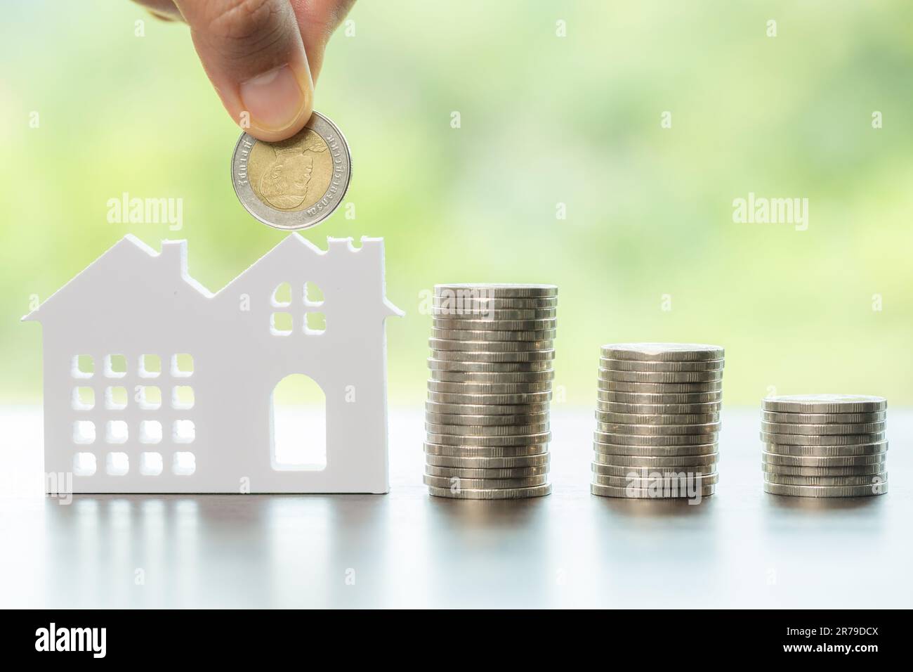 Mano che tiene monete di denaro per risparmiare per la casa residenziale. piano finanziario in contanti per prestiti o ipoteche e investimenti con banca. Concetto per assicuratore della casa Foto Stock