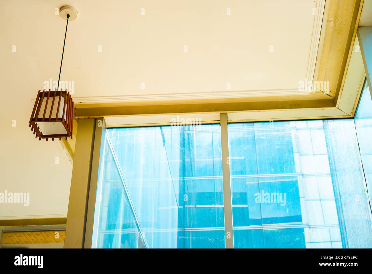 Lampada a sospensione dall'estetica serena contro un'ampia finestra in vetro in un'alta struttura. Accattivante fusione di atmosfera gialla e blu Foto Stock