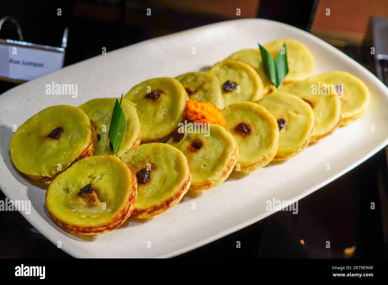 Serve il "Kue Lumpur" su un piatto di ceramica bianca adornato con foglie di panda e un pezzo centrale di contorno dell'uva passa Foto Stock