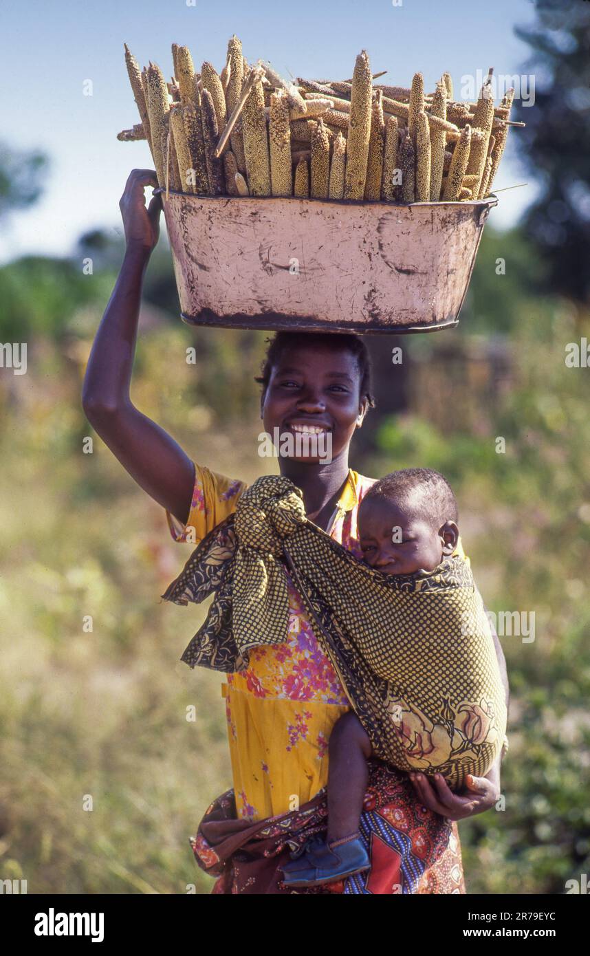 Zambia, donna con il bambino in una fionda, riporta il raccolto di mais a casa sua. Foto Stock