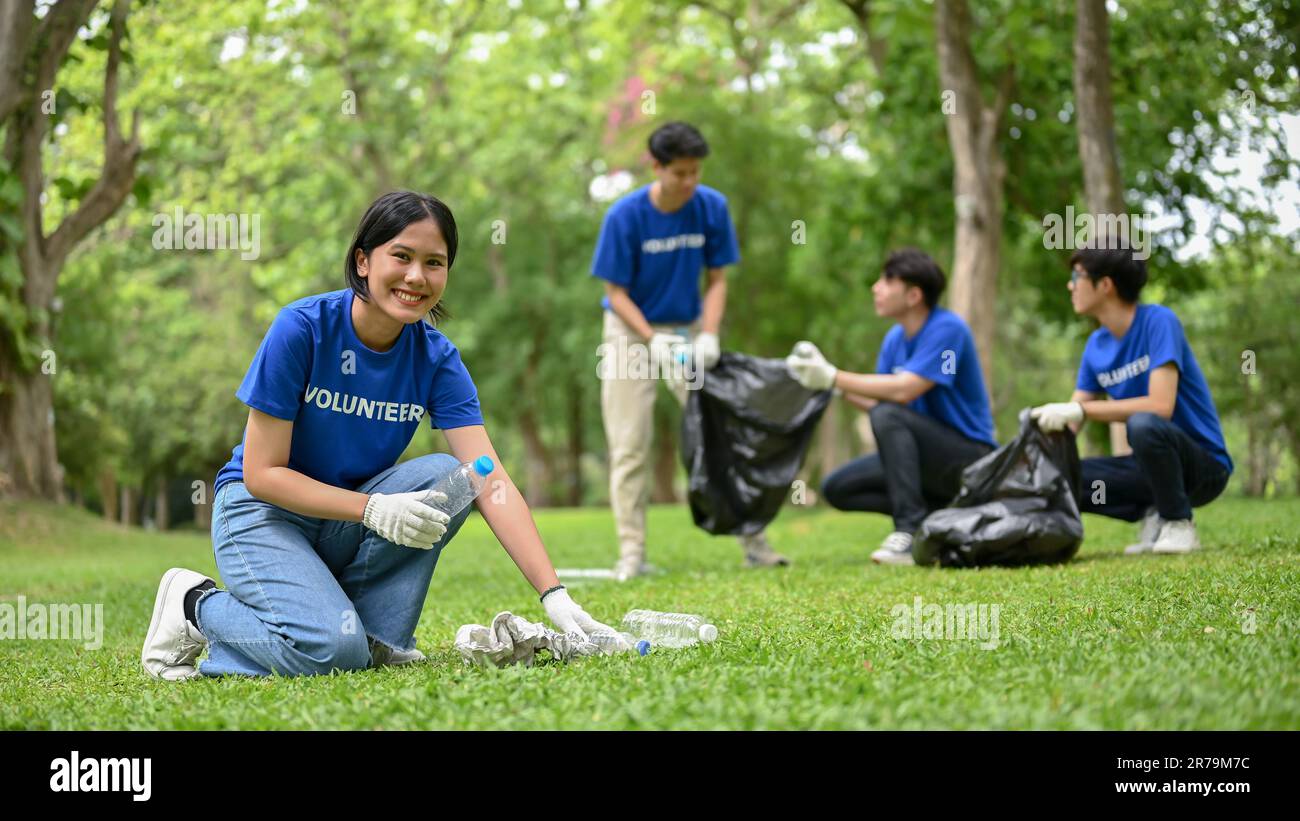 Una giovane volontaria asiatica bella e sorridente sta aiutando la sua squadra a ripulire un'area in un parco pubblico. Evento benefico, volontariato, progetto CSR Foto Stock