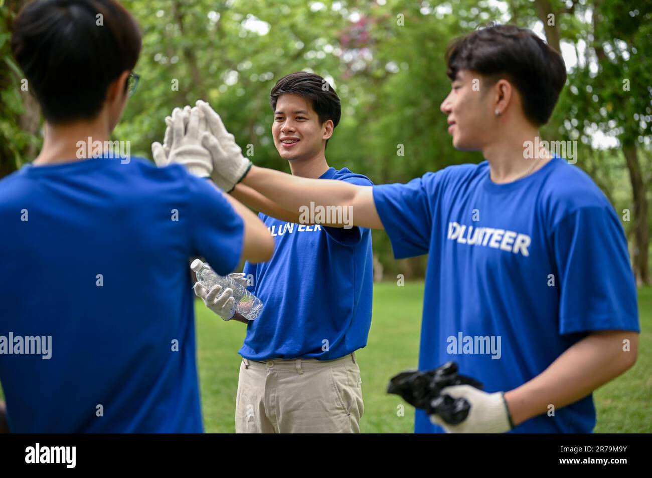 Un gruppo di giovani volontari asiatici allegri si uniscono le mani insieme o danno alti five per rallegrarsi, preparandosi a lavorare come volontari. Foto Stock