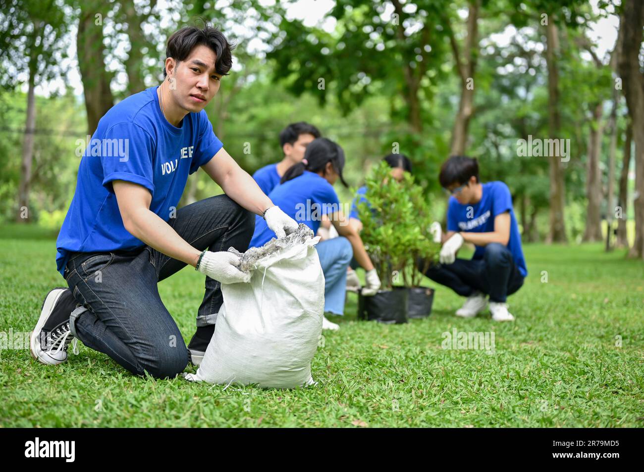 Un bel giovane e felice asiatico giovane volontario di giardinaggio maschile in un parco pubblico con la sua squadra. ecologia e sostenibilità per il concetto di comunità Foto Stock