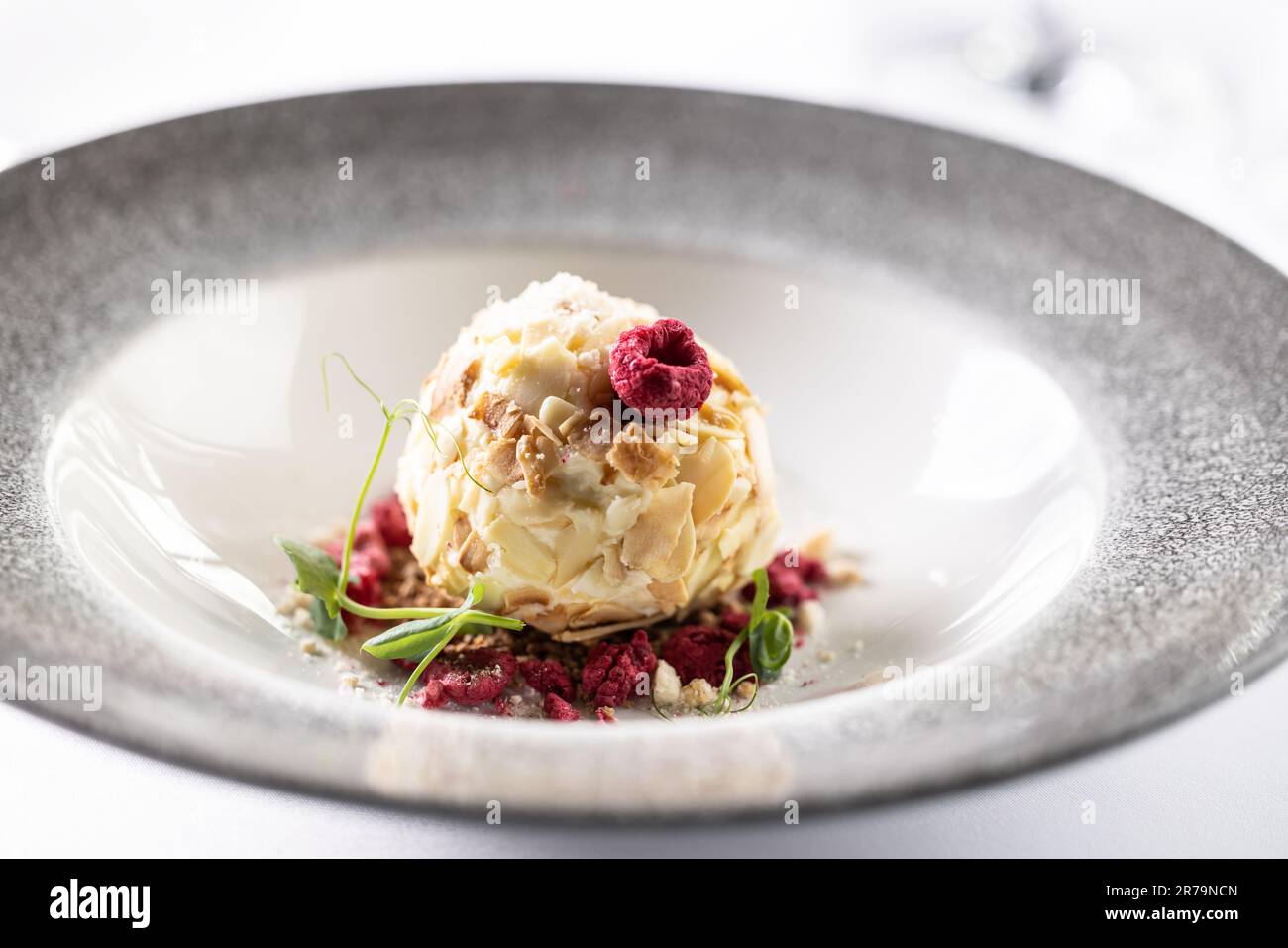 Crema di cioccolato bianco a forma di palla con frutta rossa e decorazioni verdi in un bel piatto. Foto Stock