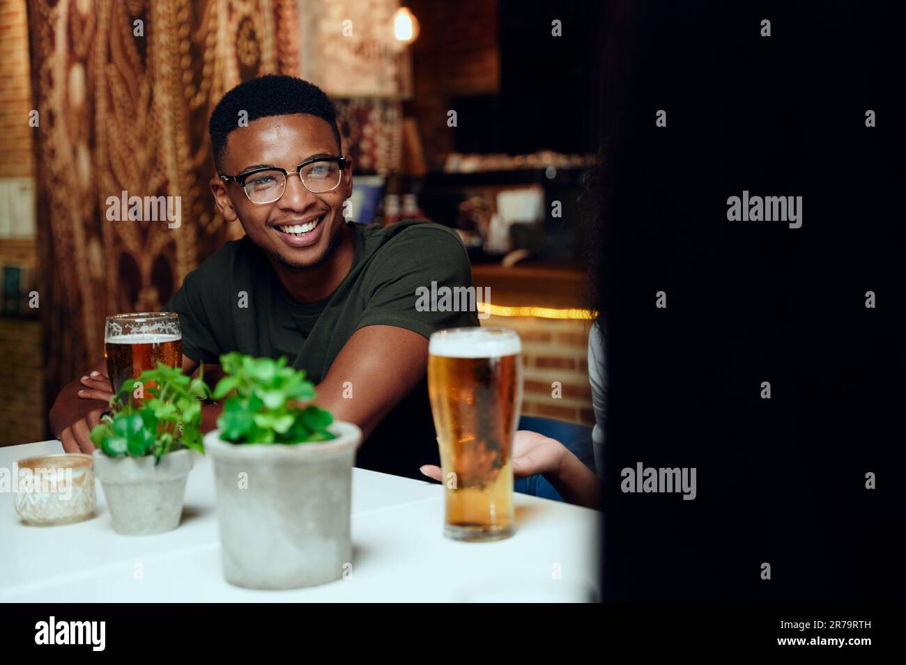 Felici giovani amici multirazziali in abbigliamento casual sorridente e gesturante con bevande al ristorante Foto Stock