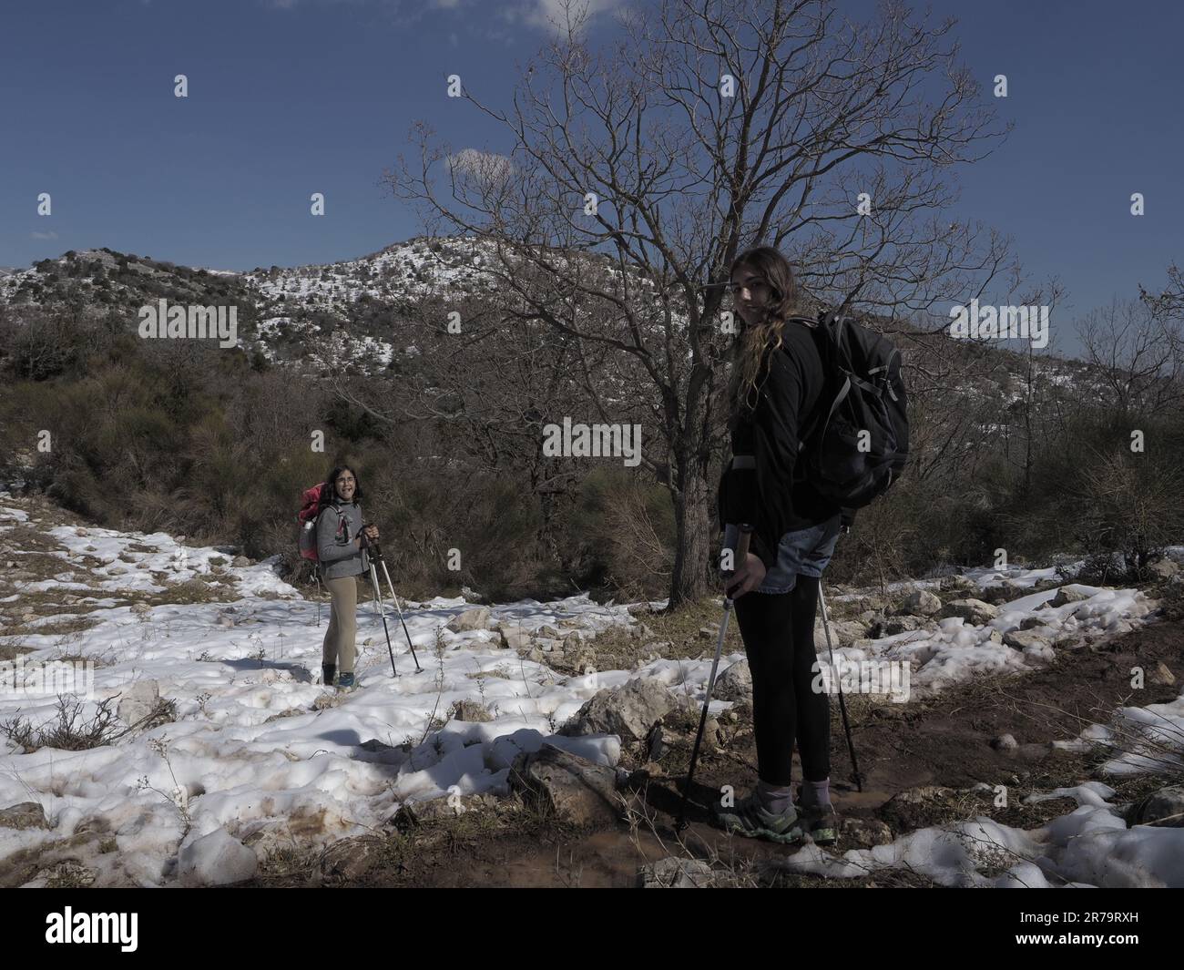 due sorelle ragazze stanno camminando sulla neve con zaino e bastoni da passeggio in una giornata limpida in montagna Foto Stock