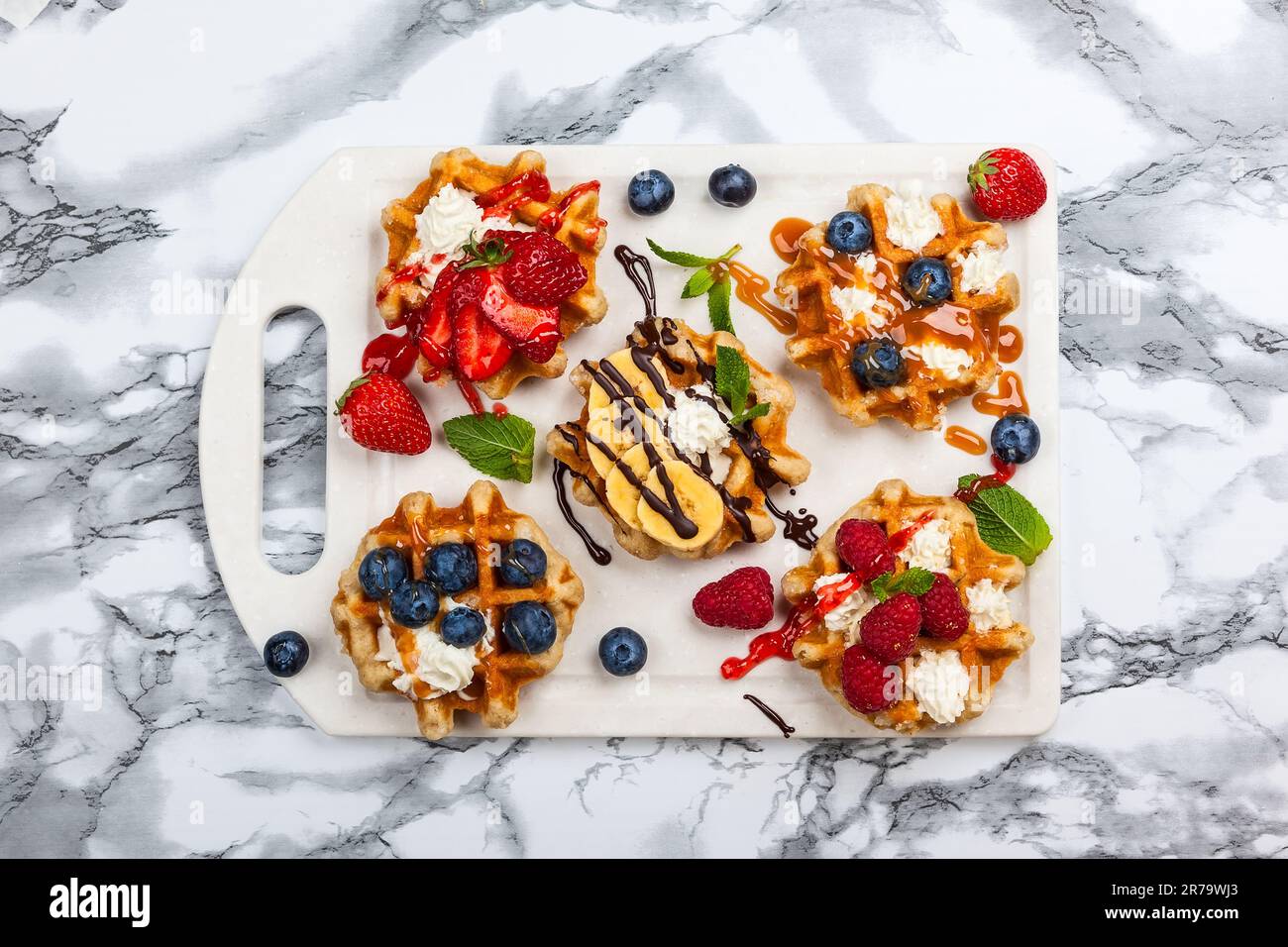 Deliziosi waffle belgi con frutti di bosco, frutta, panna montata e diversi dolcetti su marmo bianco. Vista dall'alto. Foto Stock