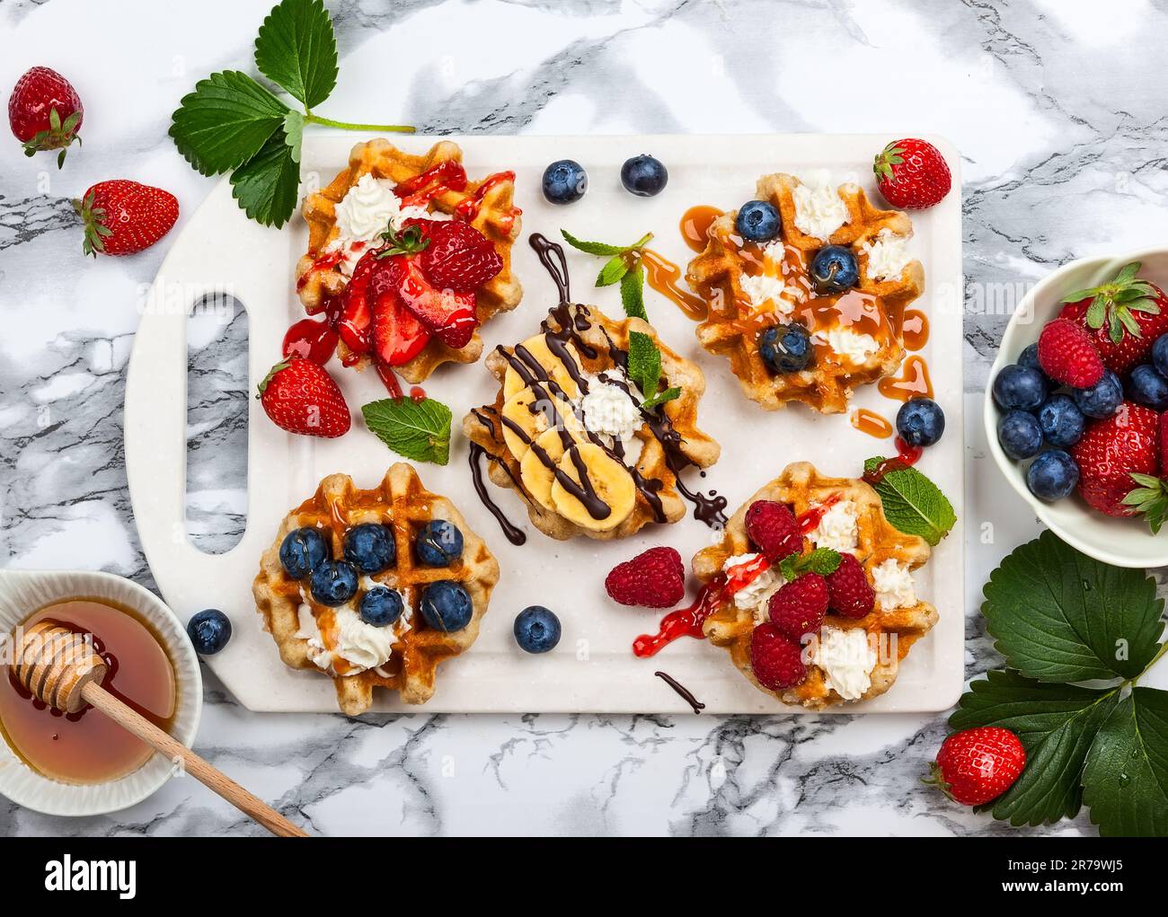 Deliziosi waffle belgi con frutti di bosco, frutta, panna montata e diversi dolcetti su marmo bianco. Vista dall'alto. Foto Stock