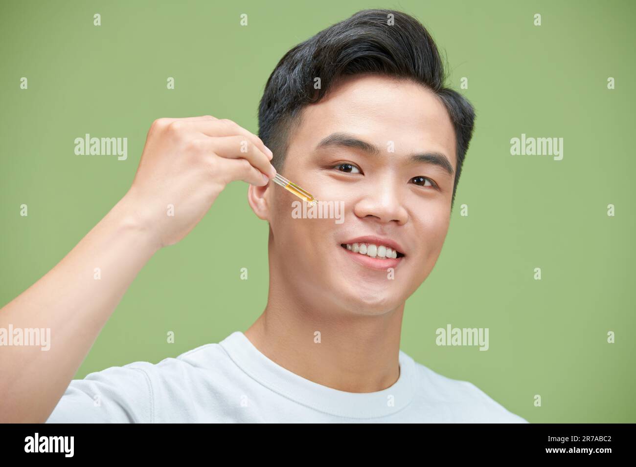 Foto dell'uomo asiatico applicare la lozione di olio di siero perfetta idratazione della pelle fresca isolato sul verde Foto Stock