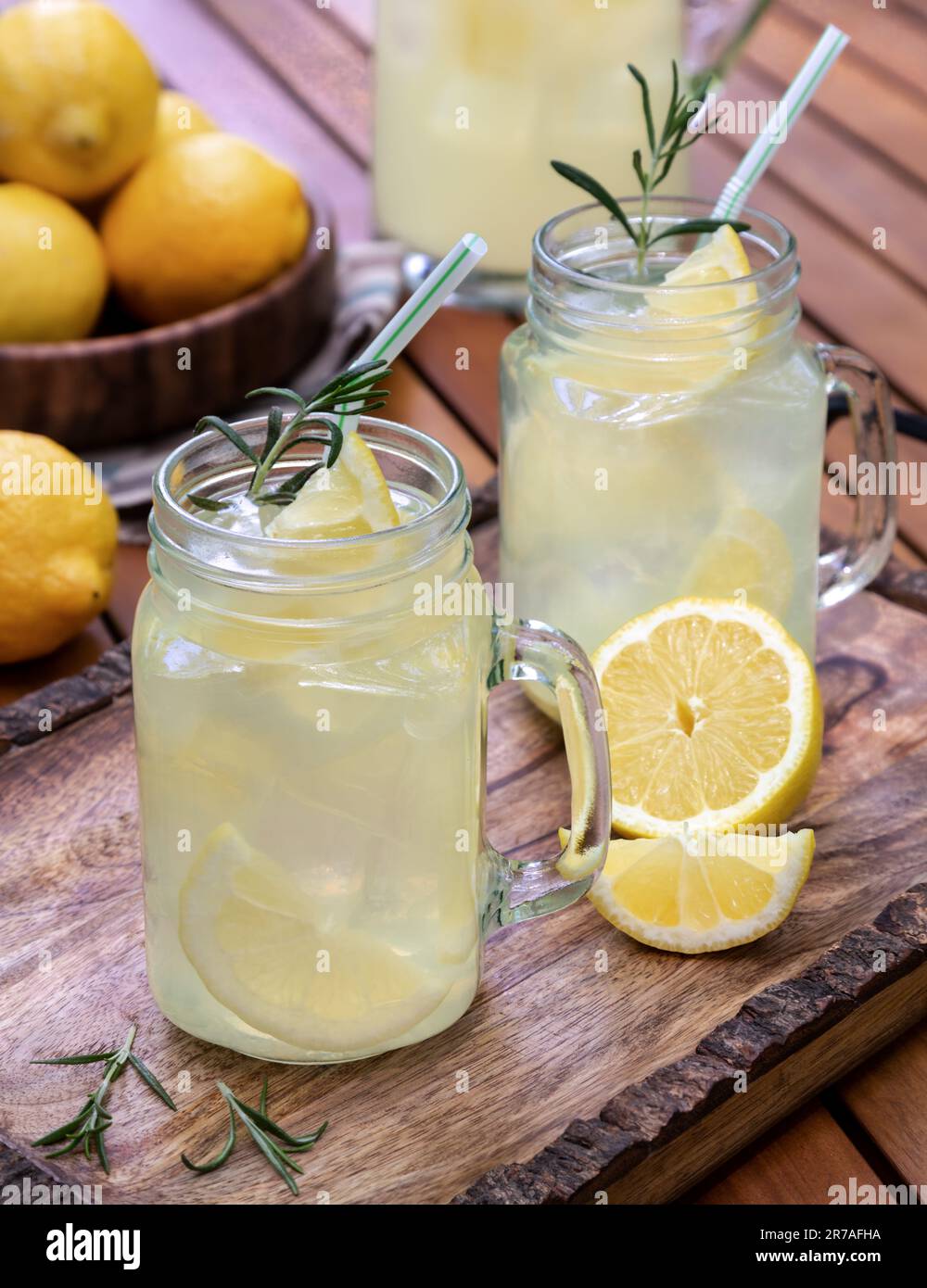 Limonata in due vasetti di vetro con limoni a fette, rosmarino e ghiaccio su un vassoio di legno Foto Stock