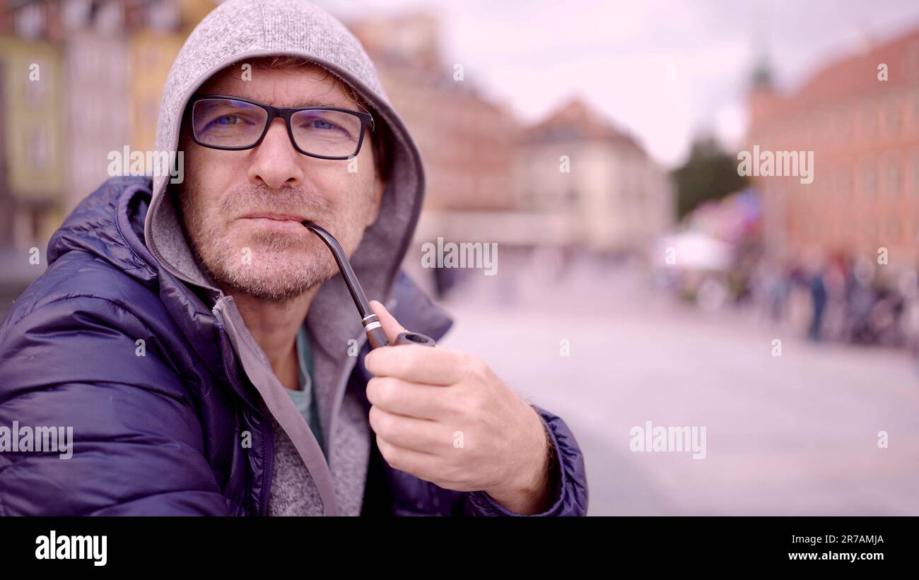 Ritratto di un uomo adulto con occhiali seduti nel cappuccio sulla piazza e fumare un tubo di tabacco nella Piazza del Palazzo, nella Città Vecchia di Varsavia Foto Stock