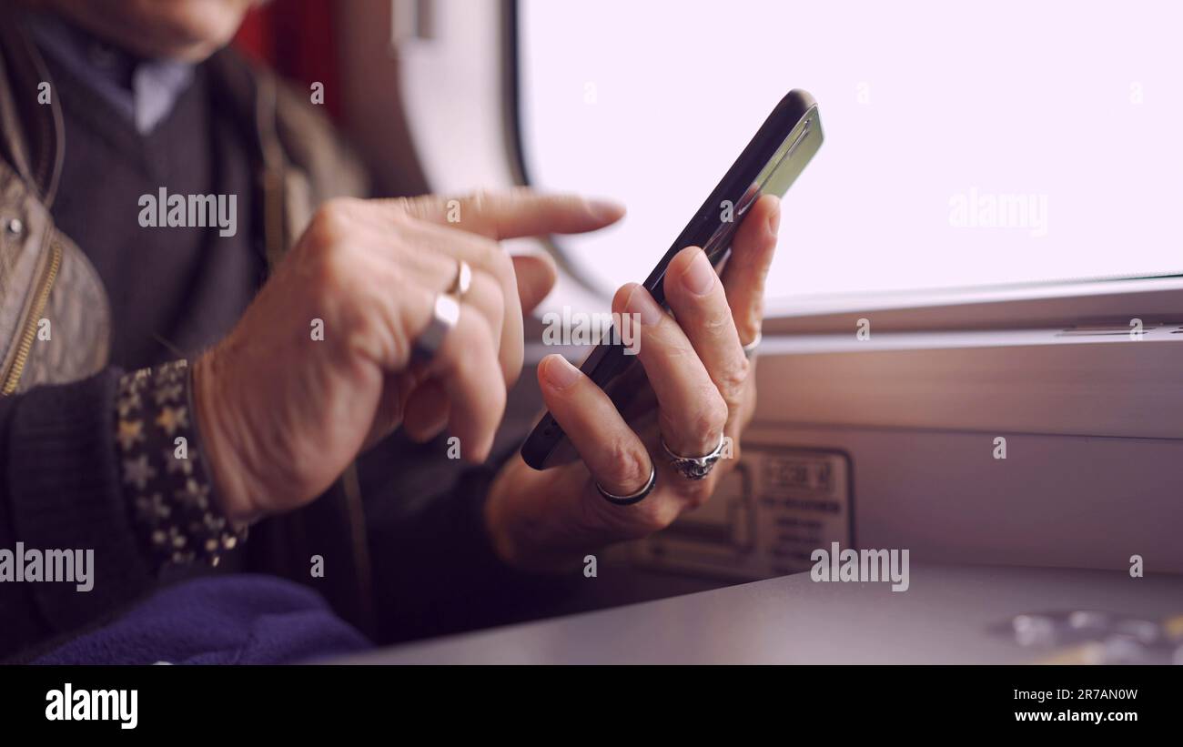 Primo piano delle mani di un anziano seduto in un carraageriage ferroviario e utilizzando uno smartphone Foto Stock