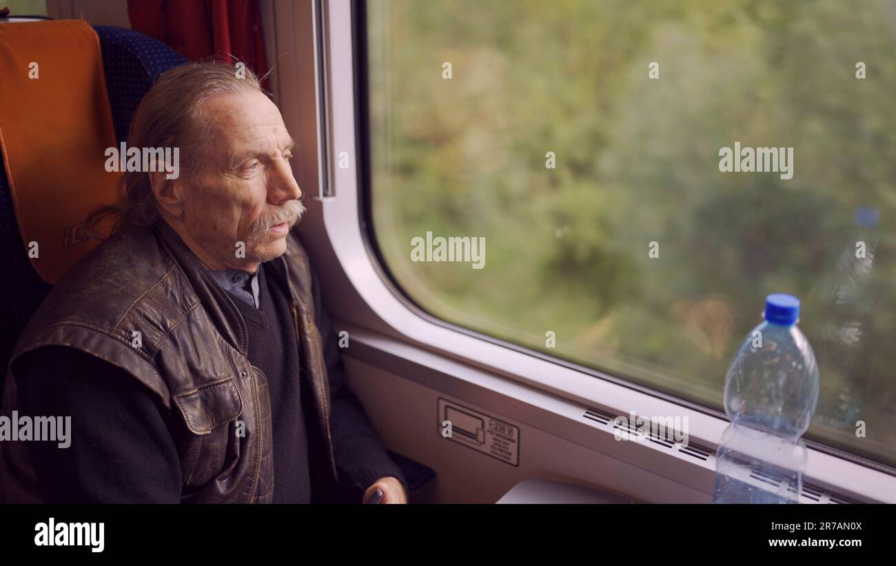 Il primo piano dell'uomo anziano con gli occhiali viaggia in treno e guarda fuori dalla finestra Foto Stock