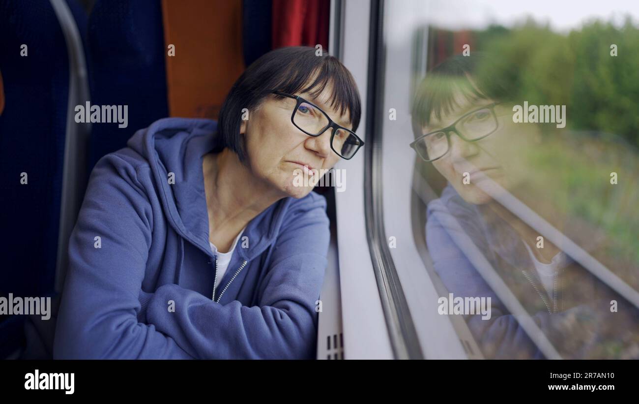 La signora anziana in vetro viaggia in treno e guarda fuori dalla finestra riflessa nel vetro Foto Stock