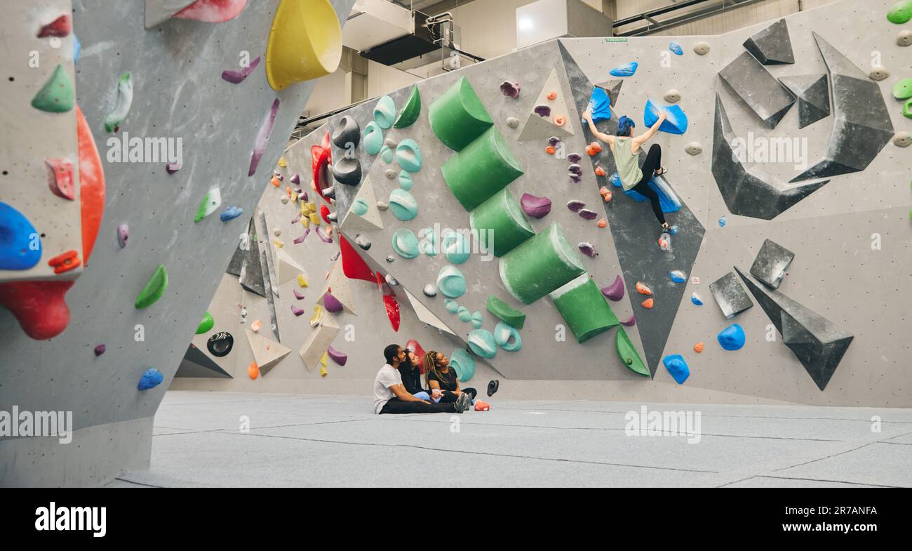 Gruppo multiculturale che guarda e incoraggia un amico sulla parete di arrampicata nel centro di attività al coperto Foto Stock
