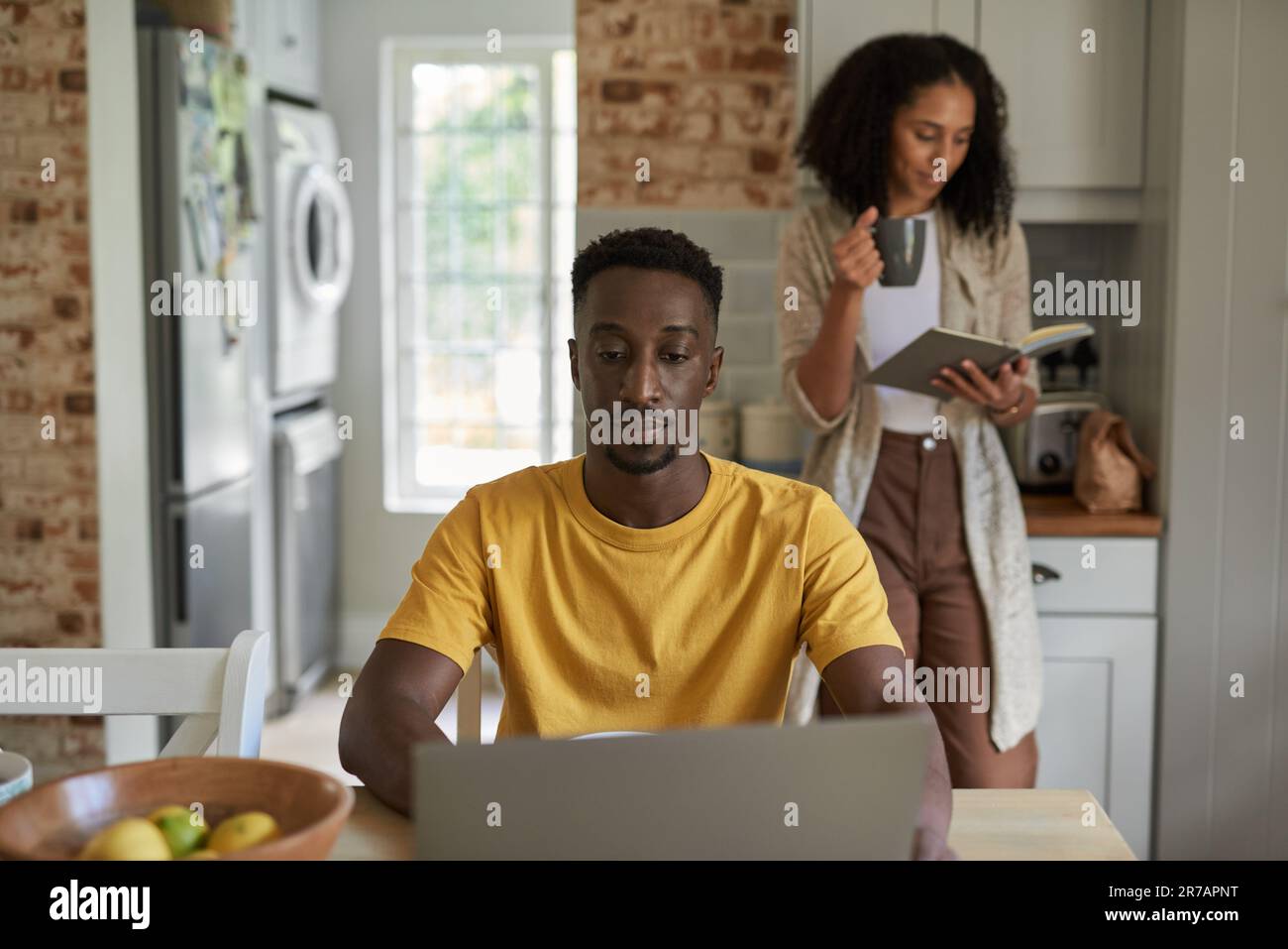 Giovane coppia multietnica che fa cose diverse durante la colazione in cucina Foto Stock