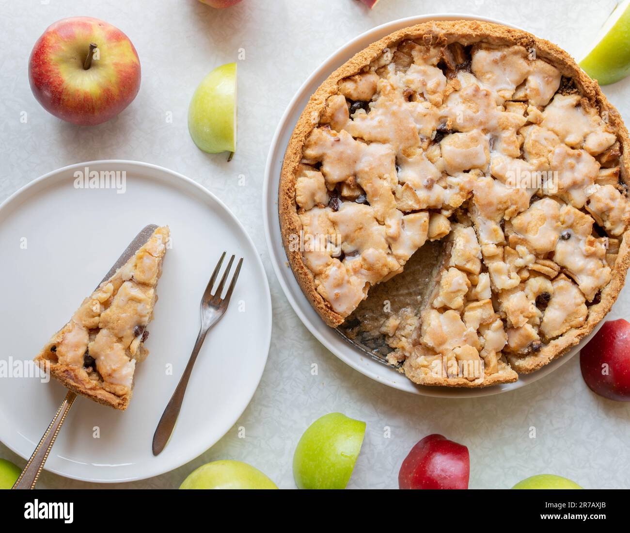 Torta di mele intere appena sfornata con cannella, ripieno di uva passa e guarnizione di glassa al limone su sfondo bianco con coloratissime decorazioni alla mela Foto Stock