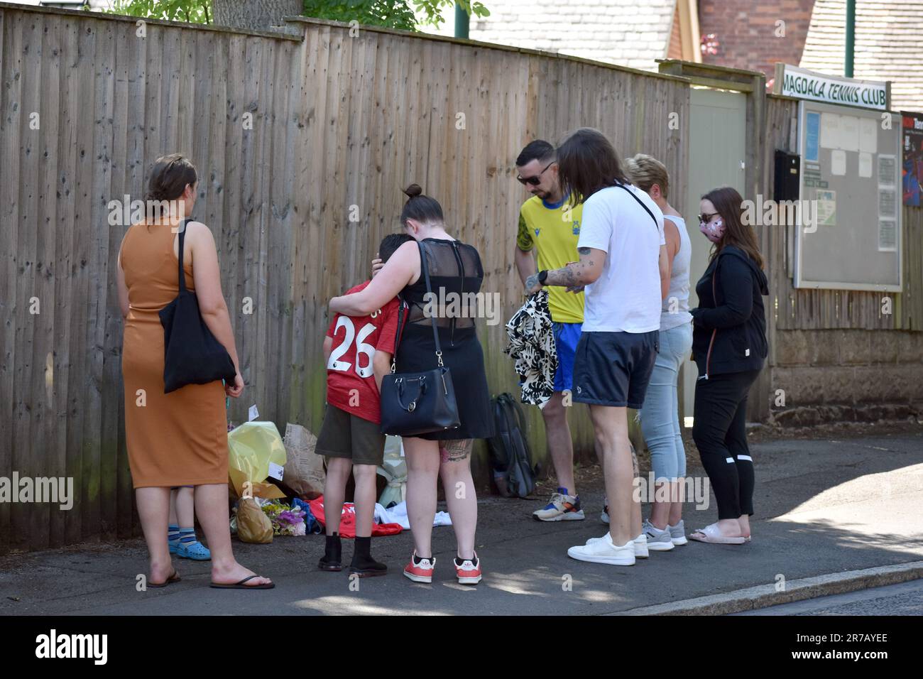 Lee Coates (parte superiore gialla) e James Coates (parte superiore bianca), i figli del custode della scuola Ian Coates, visitano la scena con altri membri della famiglia per posare i fiori e posizionare le parti superiori del calcio sul marciapiede in Magdala Road, Nottingham, dove il 65-year-old è stato trovato pugnalato. Tre persone sono state uccise e altre tre ferite in attacchi connessi il martedì mattina. Data immagine: Mercoledì 14 giugno 2023. Foto Stock