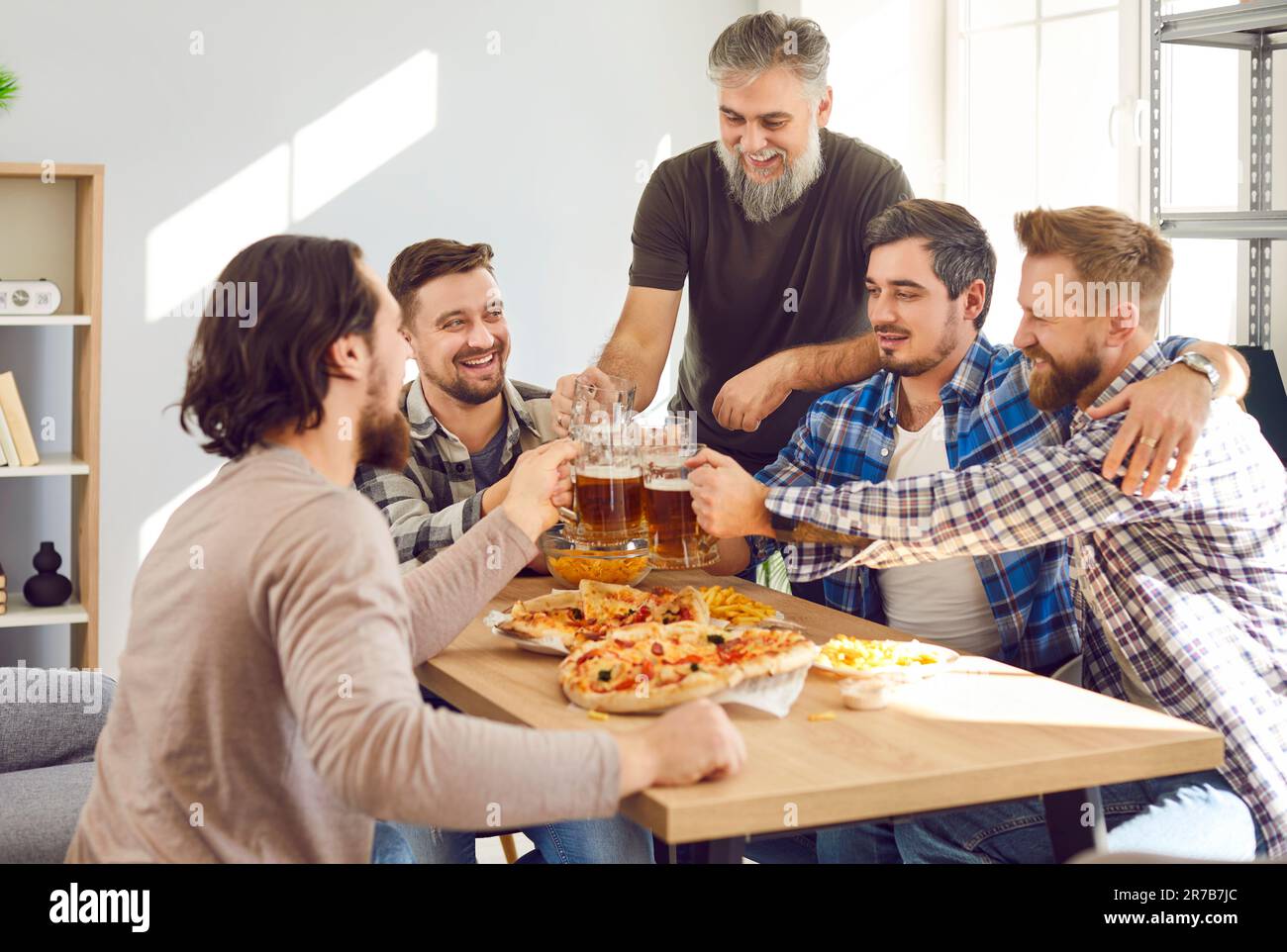 Gruppo di uomini felici seduti intorno al tavolo, bere birra, mangiare pizza e divertirsi Foto Stock