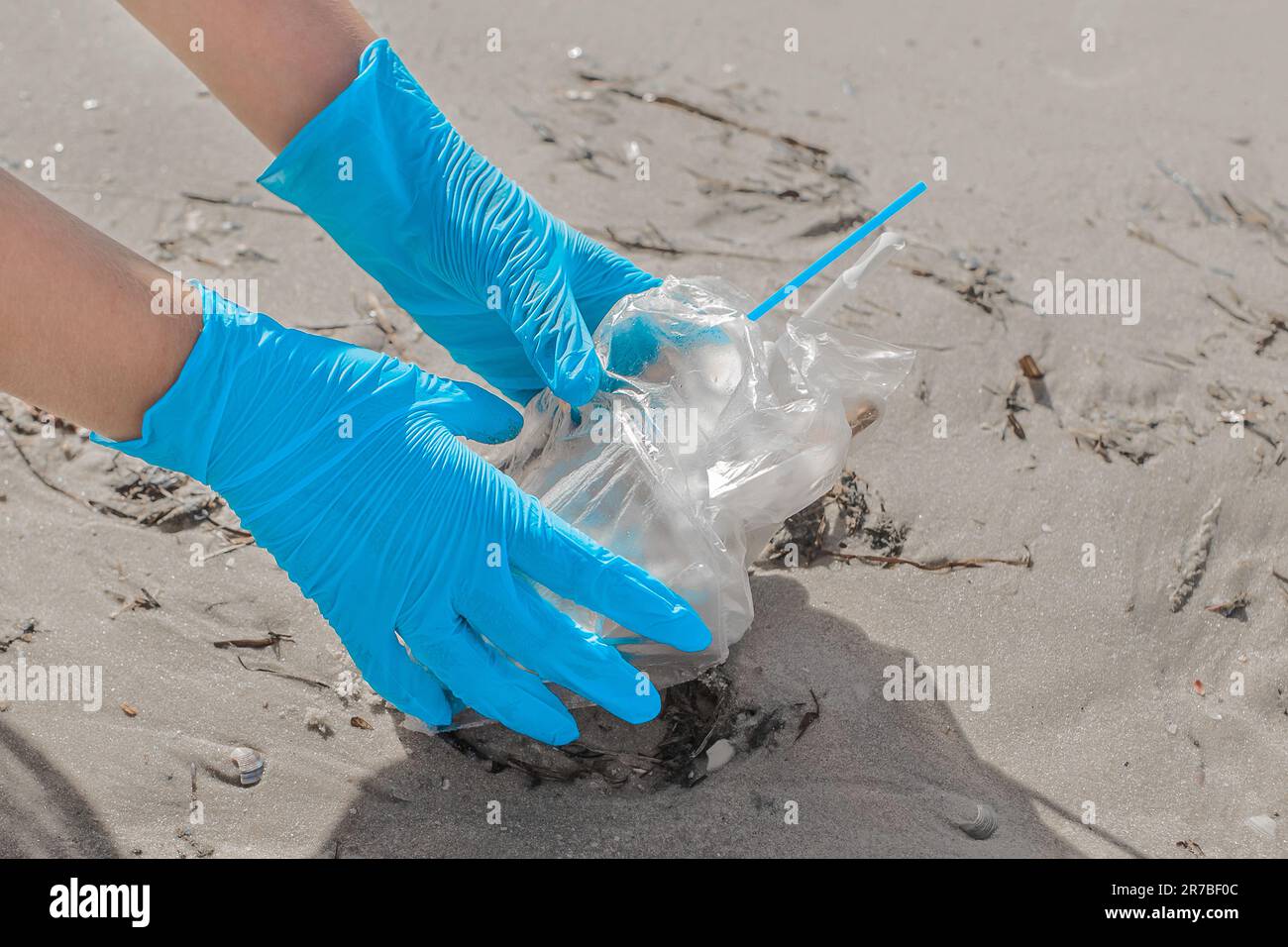 Le mani dell'uomo in guanti di protezione in lattice blu rimuovono i rifiuti sulla spiaggia. Foto Stock