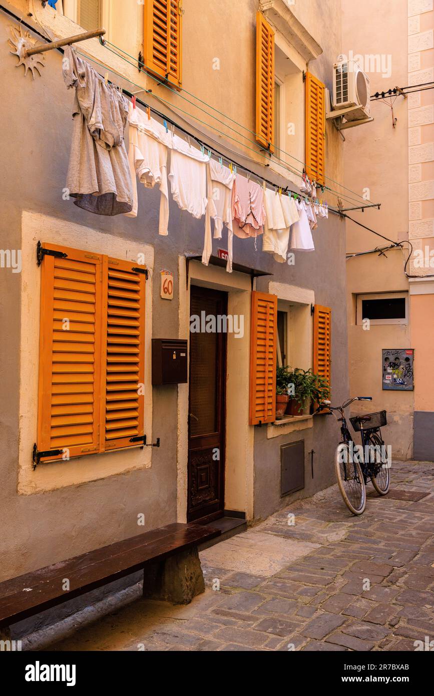 il lavaggio si appende su una linea e una vecchia bicicletta si appoggia contro una casa con le persiane gialle su una strada stretta nel centro storico di piran Foto Stock