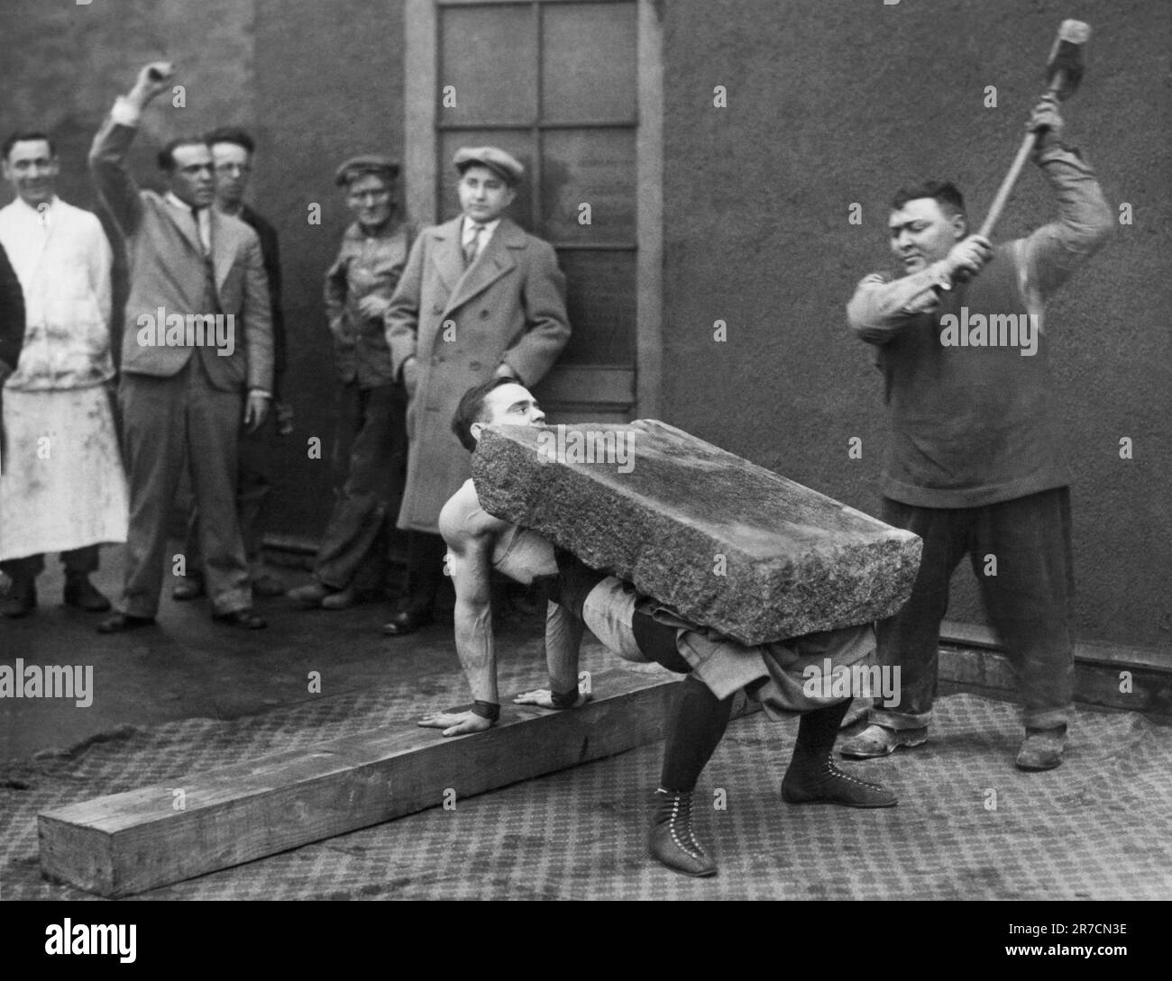 New York, New York: Il 9 aprile 1926 l'uomo forte greco, Gus Lessis, tiene una roccia di 800 libbre sul suo petto mentre un uomo la distrugge a pezzetti con un martello da slitta. Lessis intende sfidare il campione di pugilato leggero e pesante Paul Berlenbach per il titolo. Foto Stock