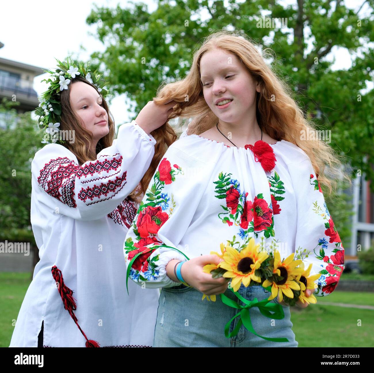 belle ragazze giovani donne tessendo corone a piedi ridendo chiacchierare nel parco in giardino ricamato nazionale camicie ucraine corone di girasole fiori e foresta fiori bianchi bella vyshyvanka Foto Stock