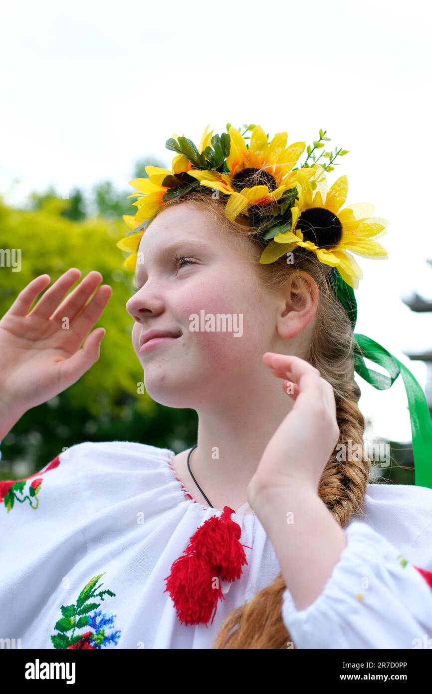 Giovane ragazza dai capelli rossi in una corona di girasoli all'aperto nel giardino del parco in bella maglietta Ucraina ricamata vyshyvanka con treccia rossa con nastri Ucraina tempo pacifico di felicità gioia e pace Foto Stock