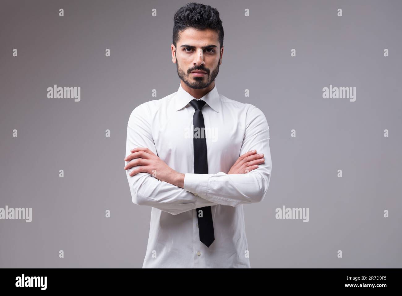 Un uomo d'affari serio e determinato in una camicia bianca, cravatta nera, braccia incrociate. Quasi arrabbiato, la sua carnagione scura e la barba ben curata completano l'hal Foto Stock