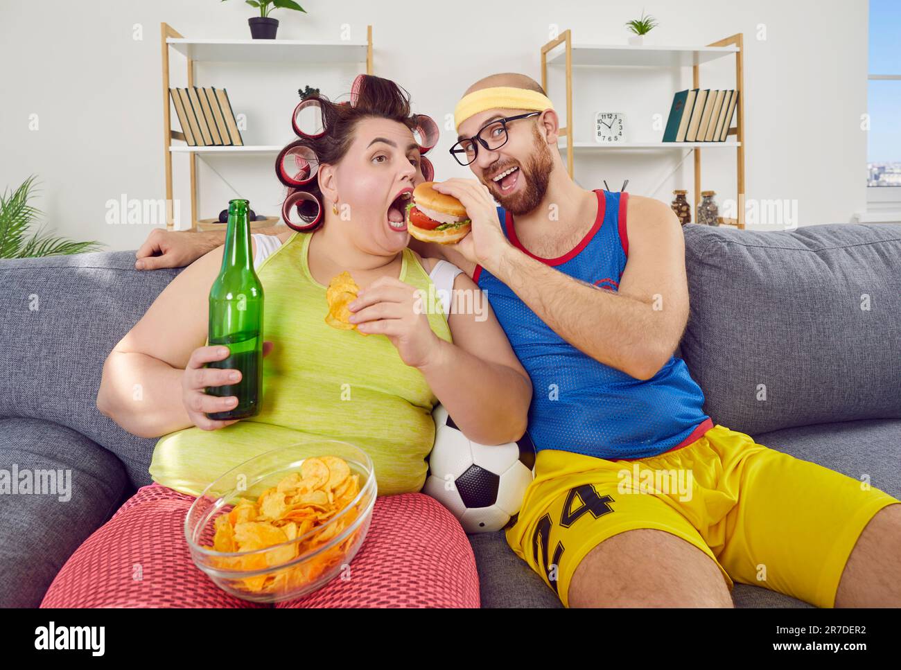 Divertente uomo e donna grassa che hanno cheat giorno, seduta sul divano e mangiare cibo malsano Foto Stock