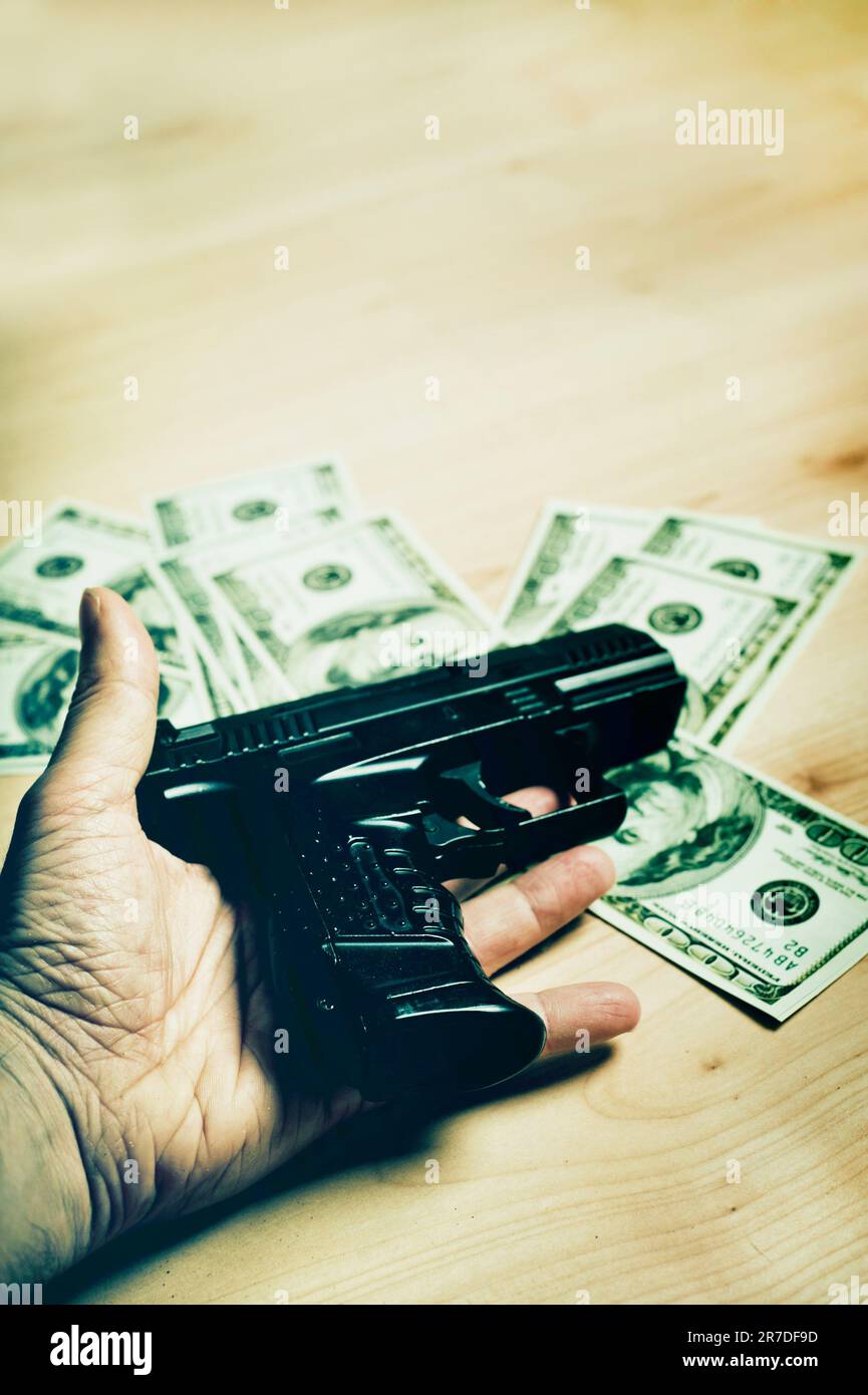 mano sdraiata a terra con una pistola e banconote in dollari Foto Stock