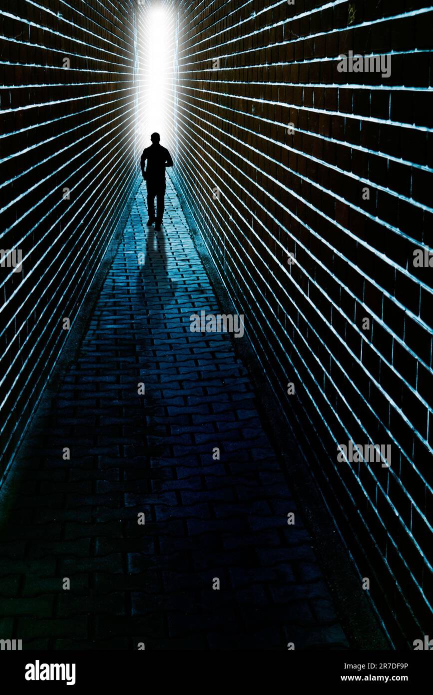 misterioso uomo in nero che corre in strada tra due alte mura Foto Stock