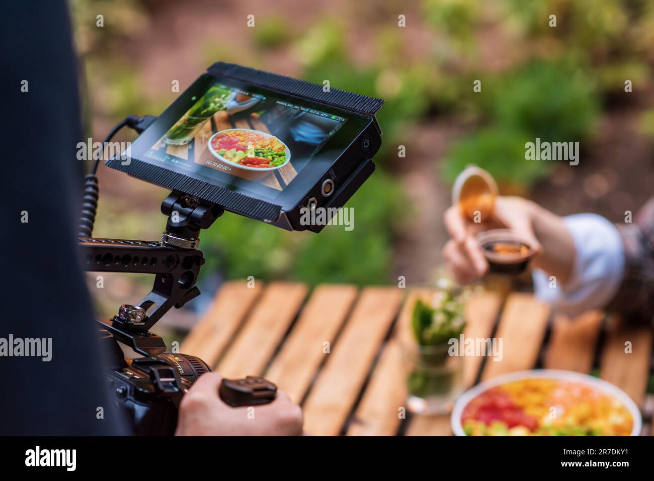 Vista ravvicinata di un fotografo che fotografa un poke Bowl su una fotocamera professionale con display esterno in un parco Foto Stock