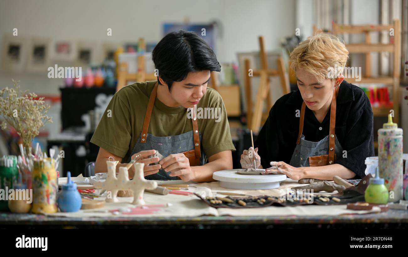 Due giovani uomini asiatici si uniscono a un laboratorio artigianale e amano fare ornamenti di argilla o terracotta nel laboratorio insieme. Foto Stock