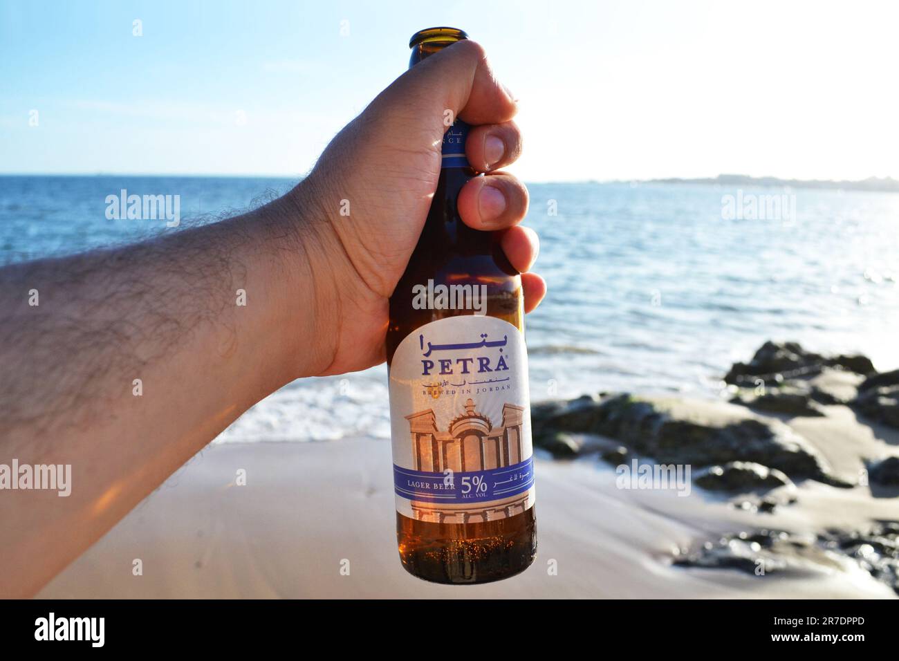 AQABA/GIORDANIA - 10th 2023 GIUGNO: Petra 33cl bottiglia di birra lager in mano vicino alla spiaggia. La birra Petra è la più antica birra locale della Giordania. Foto Stock