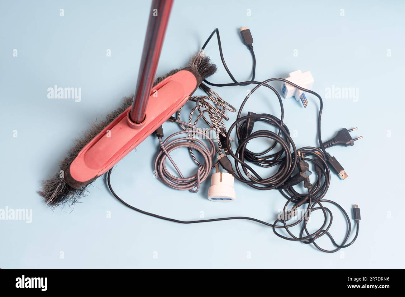 una scopa raccoglie un groviglio di vecchi cavi elettrici sul pavimento Foto Stock