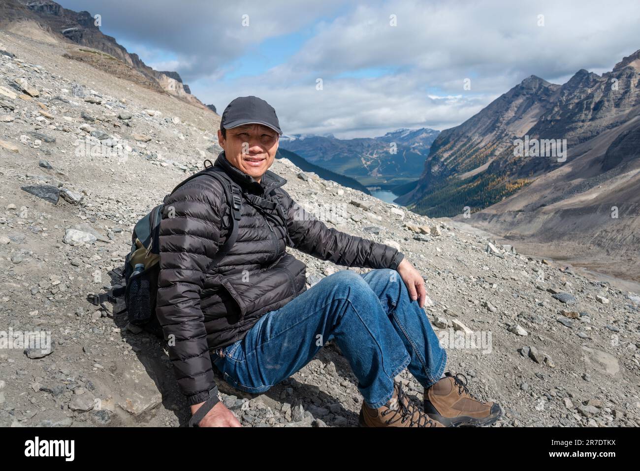 Turista seduto sul ripido pendio di rocce sciolte sulla piana di sei Glaciers pista, Lago Louise sullo sfondo. Parco Nazionale di Banff. Canada. Foto Stock