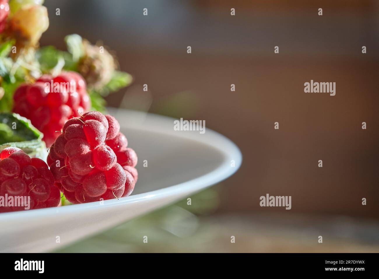 Lamponi rossi in un piatto bianco. Lamponi freschi su sfondo sfocato. Sfondo fruttato con spazio libero per il testo. Foto Stock