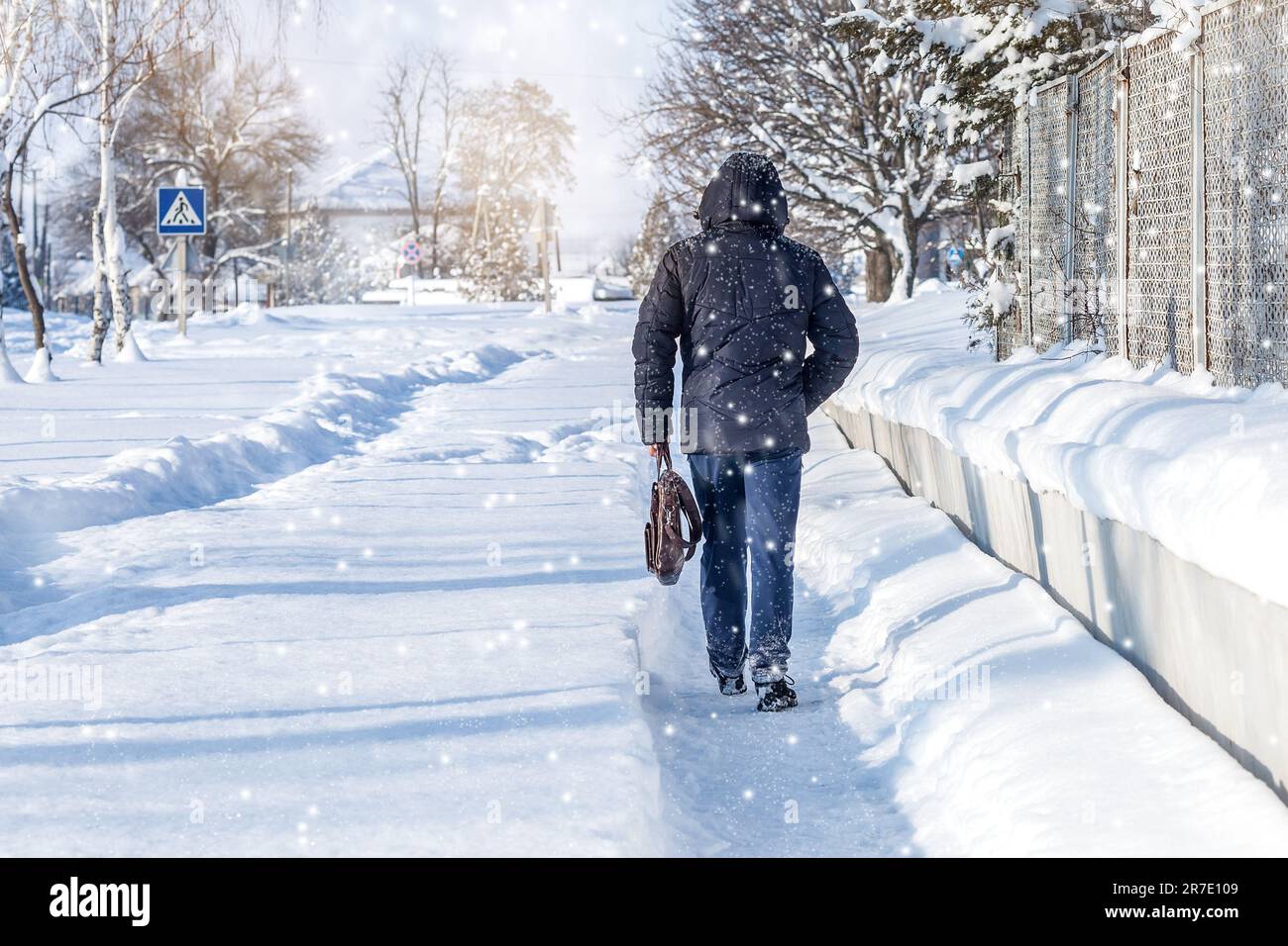 Passeggiata invernale. Un uomo in una giacca con una borsa, una passeggiata sullo sfondo di un paesaggio invernale, inverno view.A uomo cammina lungo il marciapiede durante la neve Foto Stock