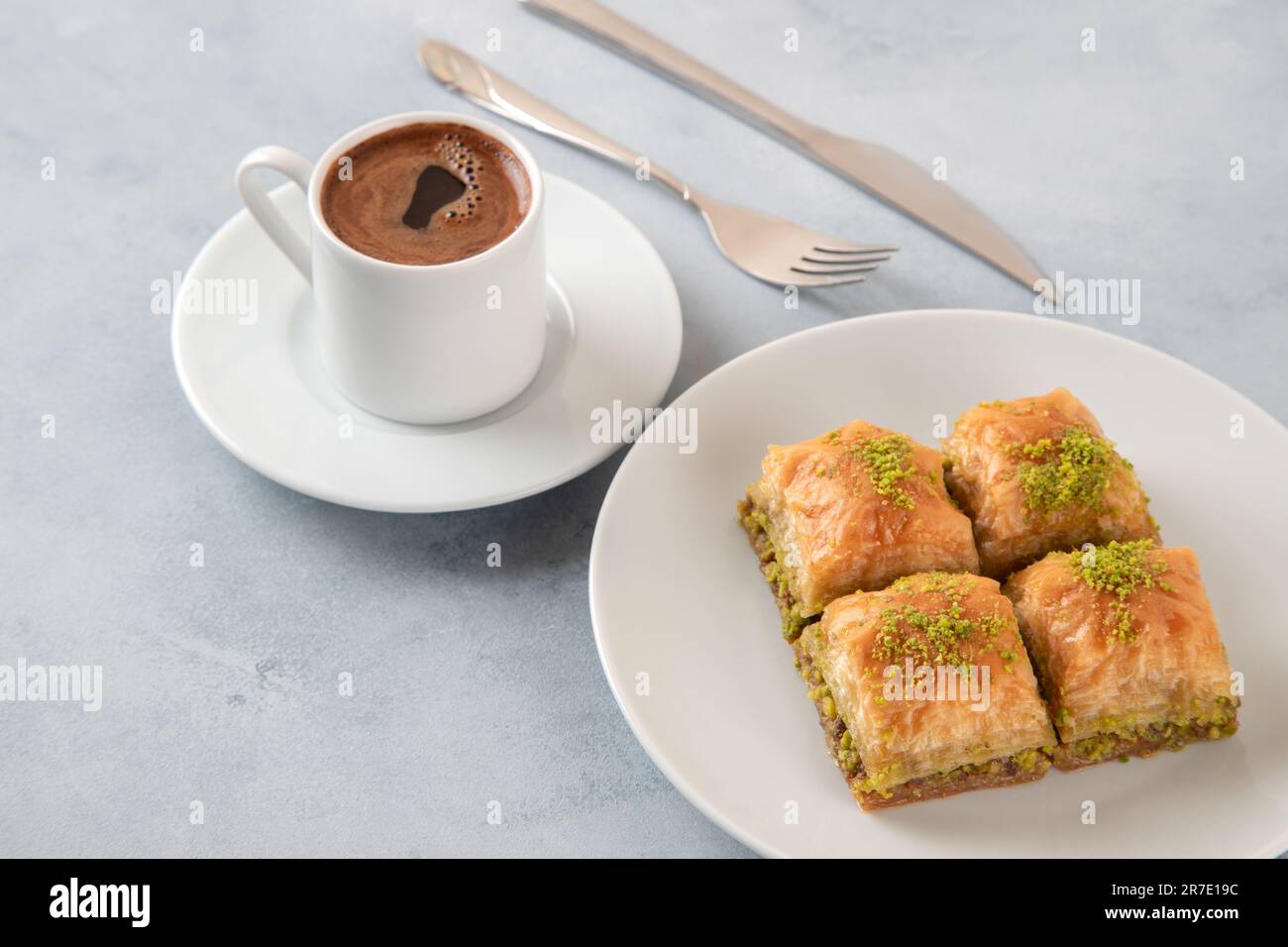 Baklava al pistacchio su un piatto bianco con caffè turco. Un piatto di baklava tradizionale su sfondo azzurro Foto Stock