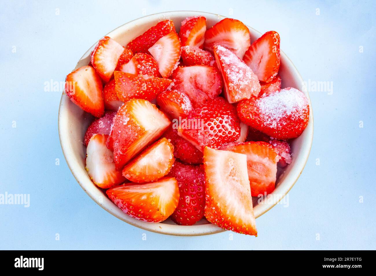 Vista ravvicinata di una ciotola di fragole fresche, affettate e cosparse di zucchero per farle macerare isolate su uno sfondo bianco Foto Stock